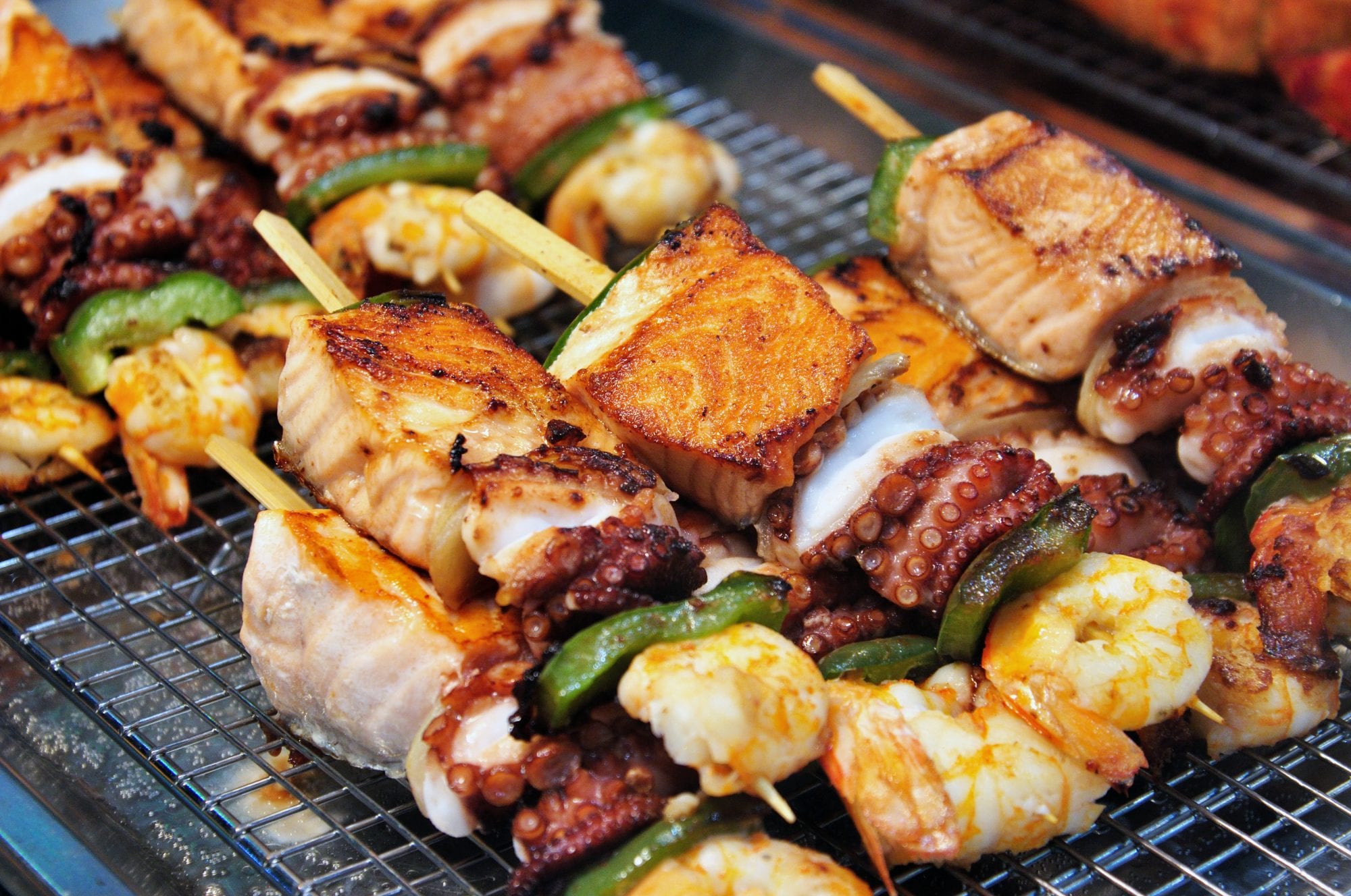 Grilled skewers of seafood consist of salmon, cuttlefish, scampi, and vegetables